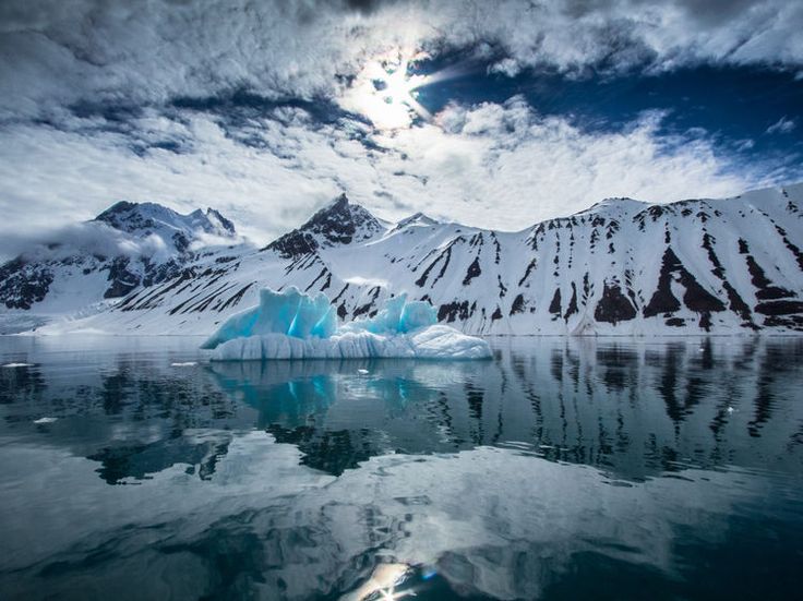 Icebergs reflected in still Arctic water beneath snow-covered peaks