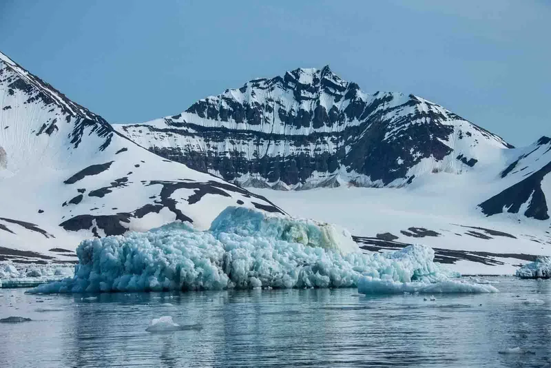 An iceberg floating near snow-covered mountains